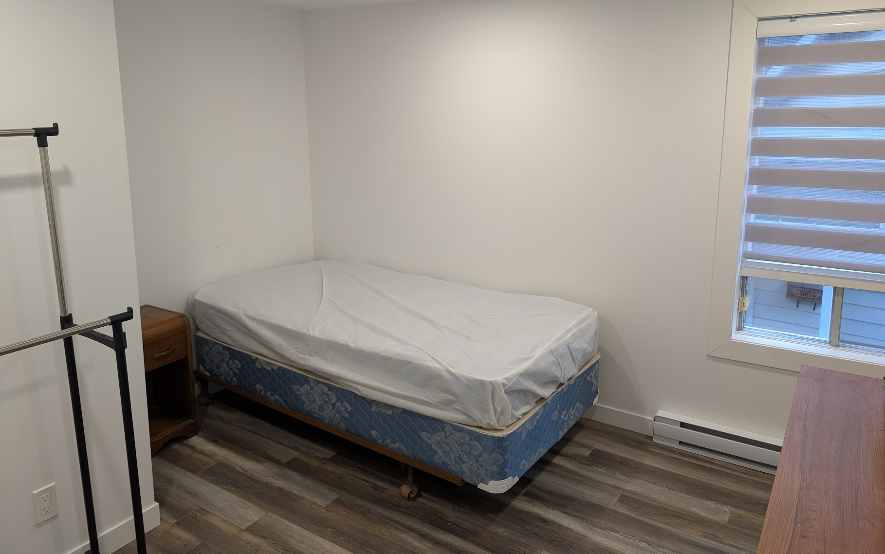 Chambre avec lit simple, table de chevet, support de rangement et une fenêtre